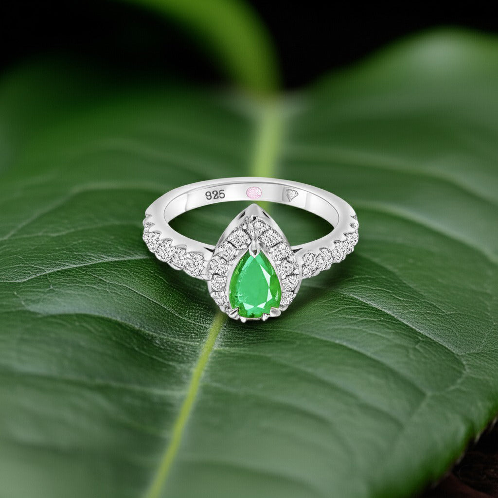 Cavell Drop of Passion natural emerald ring in sterling silver surrounded by round-cut cubic zirconia accents placed on a surface