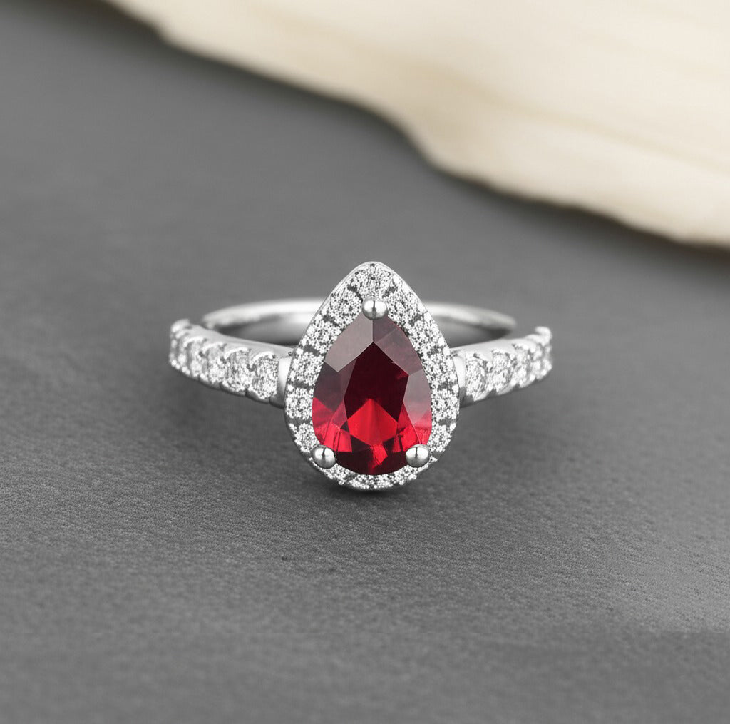 Cavell Drop of Passion natural ruby ring in sterling silver surrounded by round-cut cubic zirconia accents placed on a surface