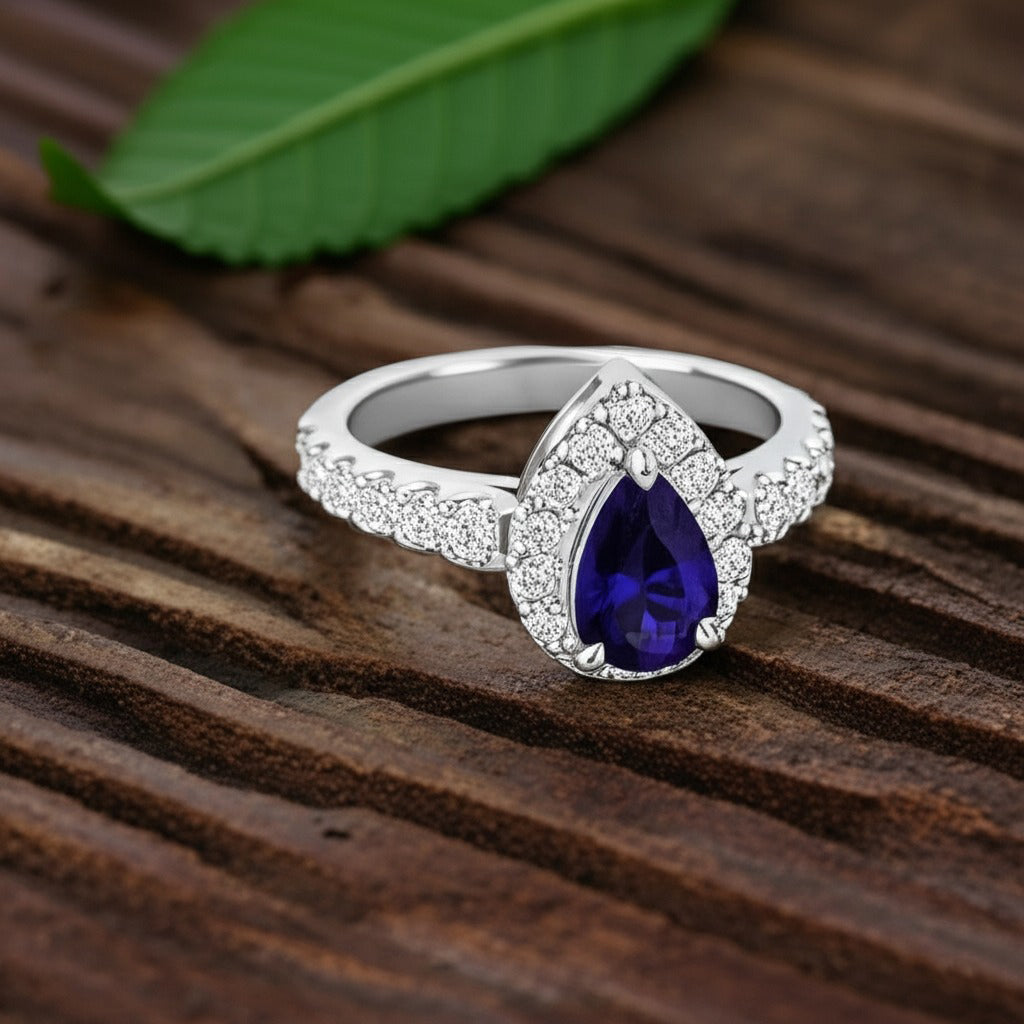 Cavell Drop of Passion natural sapphire ring in sterling silver surrounded by round-cut cubic zirconia accents placed on a surface